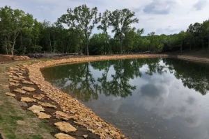Completed And Filled Pond/Lake Installation - rip rap seen in this image helps prevent soil erosion - how to build a dam for a pond