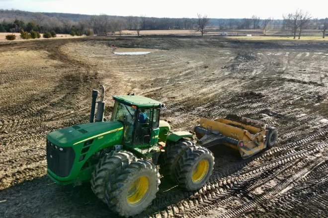 DIY pond cost can often cost more than hiring a professional due to expensive equipment rentals, such as the tractor and scraper seen in the image.