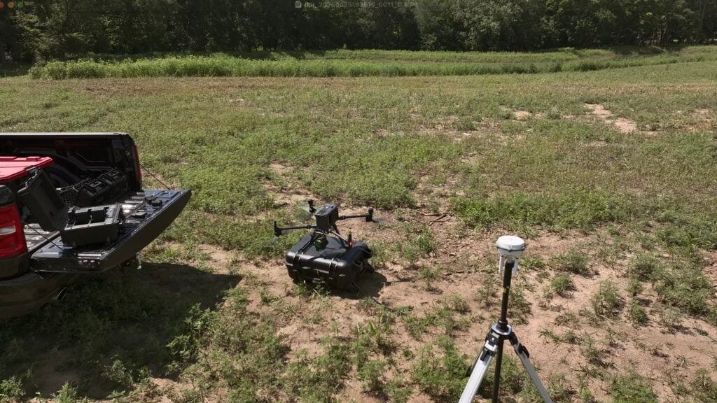 LiDAR Drone Surveying for Ponds and Lakes for Accurate Professional Planning by Bulletproof Pond and Lake.jpeg - Bulletproof Pond and Lake Open pickup bed with equipment case, drone controller, and gear on a grassy field with trees in the background, ready for a flight.