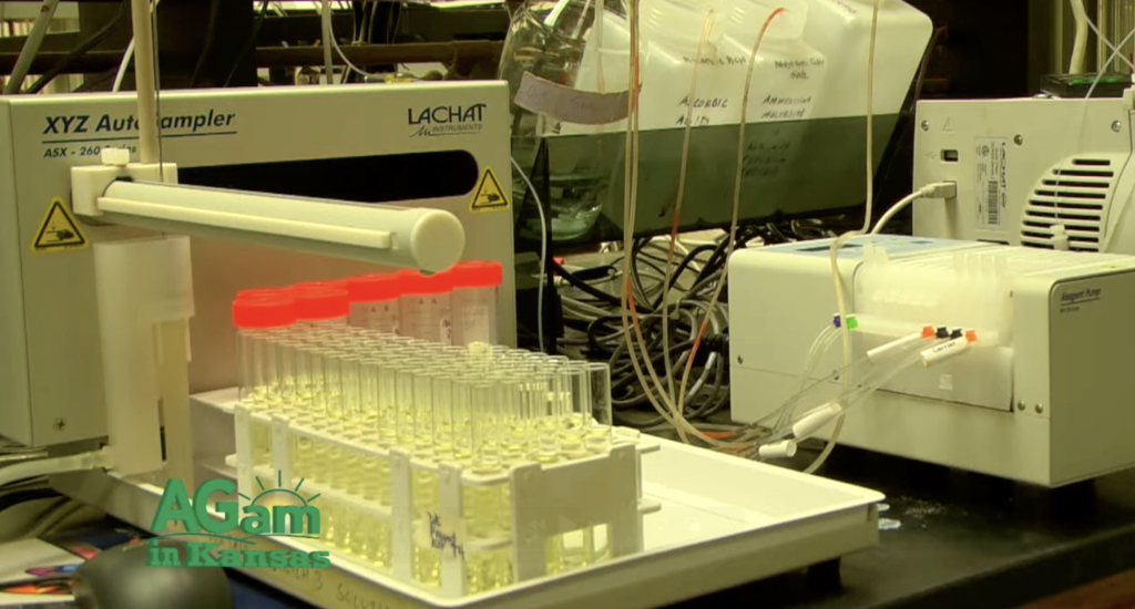 Soil testing in Labs at KState University - Bulletproof Pond and Lake Laboratory bench with a rack of red-capped test tubes and automated analytical equipment in the background with tangled cables.",