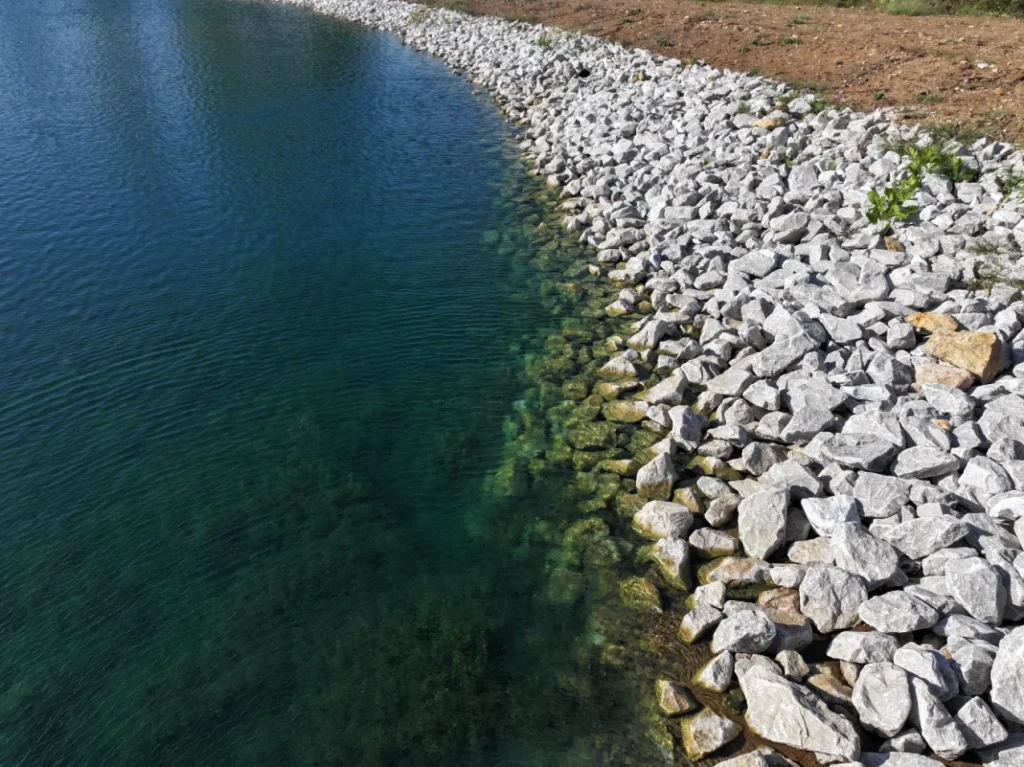 Close-up of a riprap shoreline protecting a newly built pond in Grain Valley, MO, designed by Bulletproof Pond and Lake for long-term erosion control and water clarity.