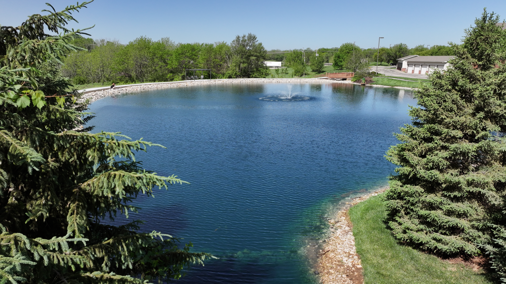 Pond Makeover with concrete walkway and treed landscaping with fountain, bridge, and fish feeder in Olathe Kansas. Completed by Bulletproof Pond and Lake