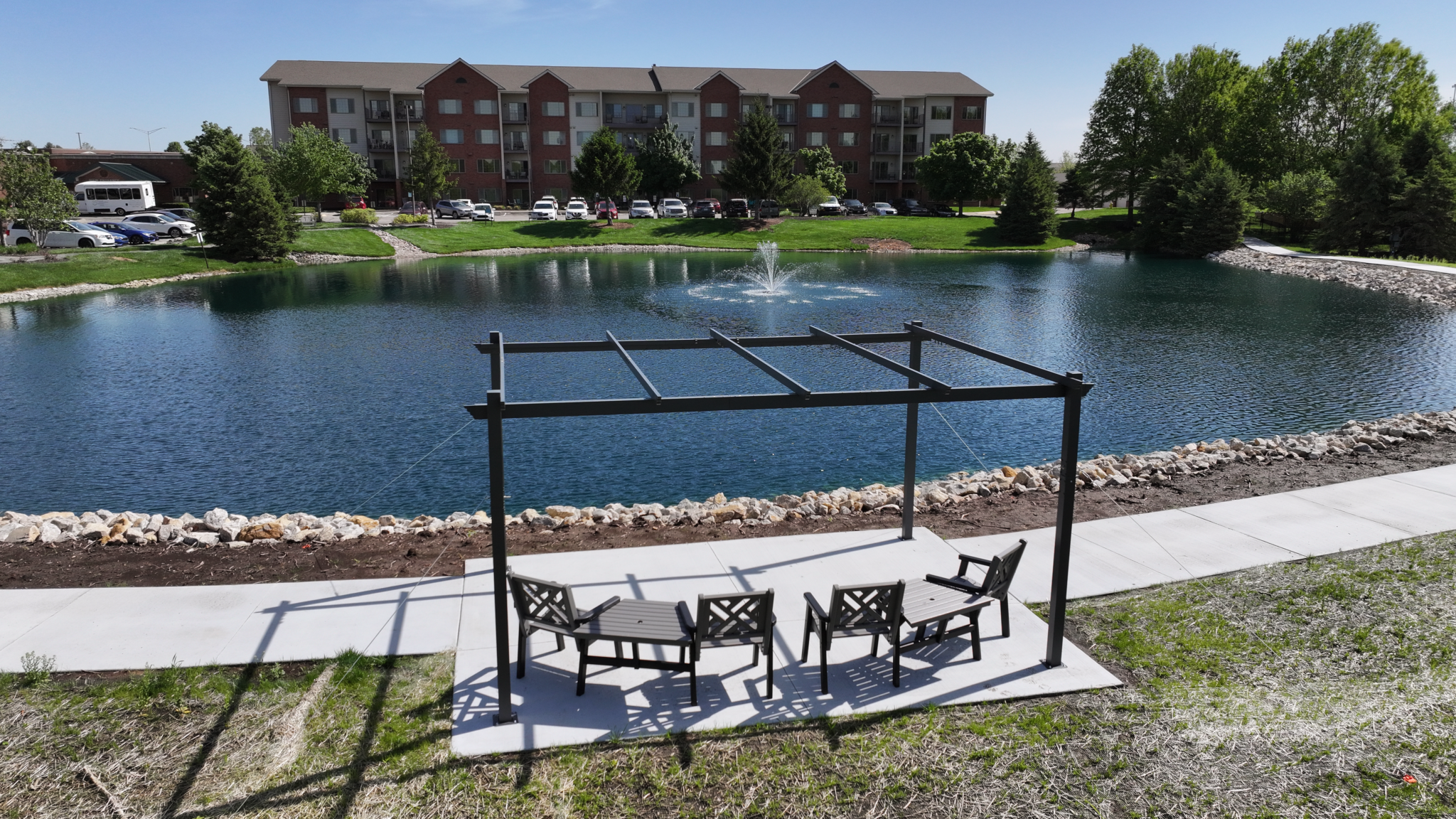 Pond Makeover with concrete walkway, entertaining space, and treed landscaping with fountain, bridge, and fish feeder in Olathe Kansas. Completed by Bulletproof Pond and Lake