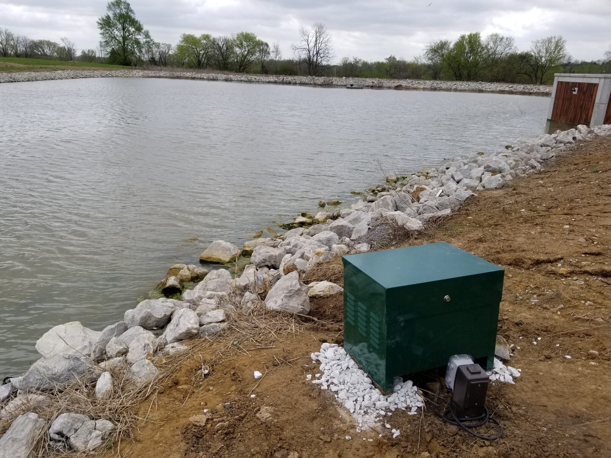 Pond aeration system compressor cabinet beside a riprap-lined pond in Missouri, installed by Midwest Lake Management