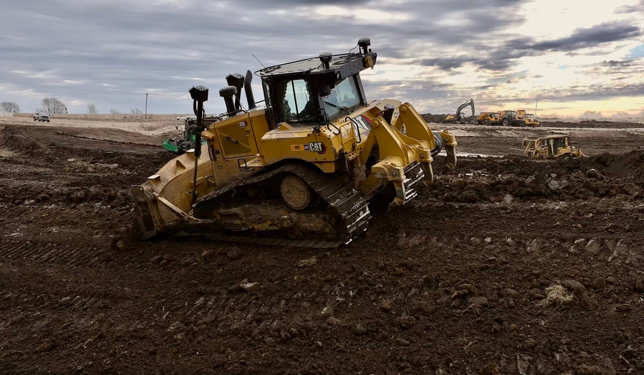GPS-guided dozer grading a large pond and lake construction site, with an excavator, haul trucks and a scraper working behind it