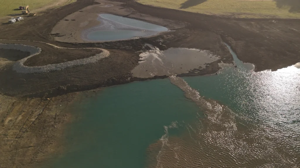 Existing pond water flowing through a breach in the old dam into a new lake expansion built by Bulletproof Pond and Lake in Melvern, Kansas