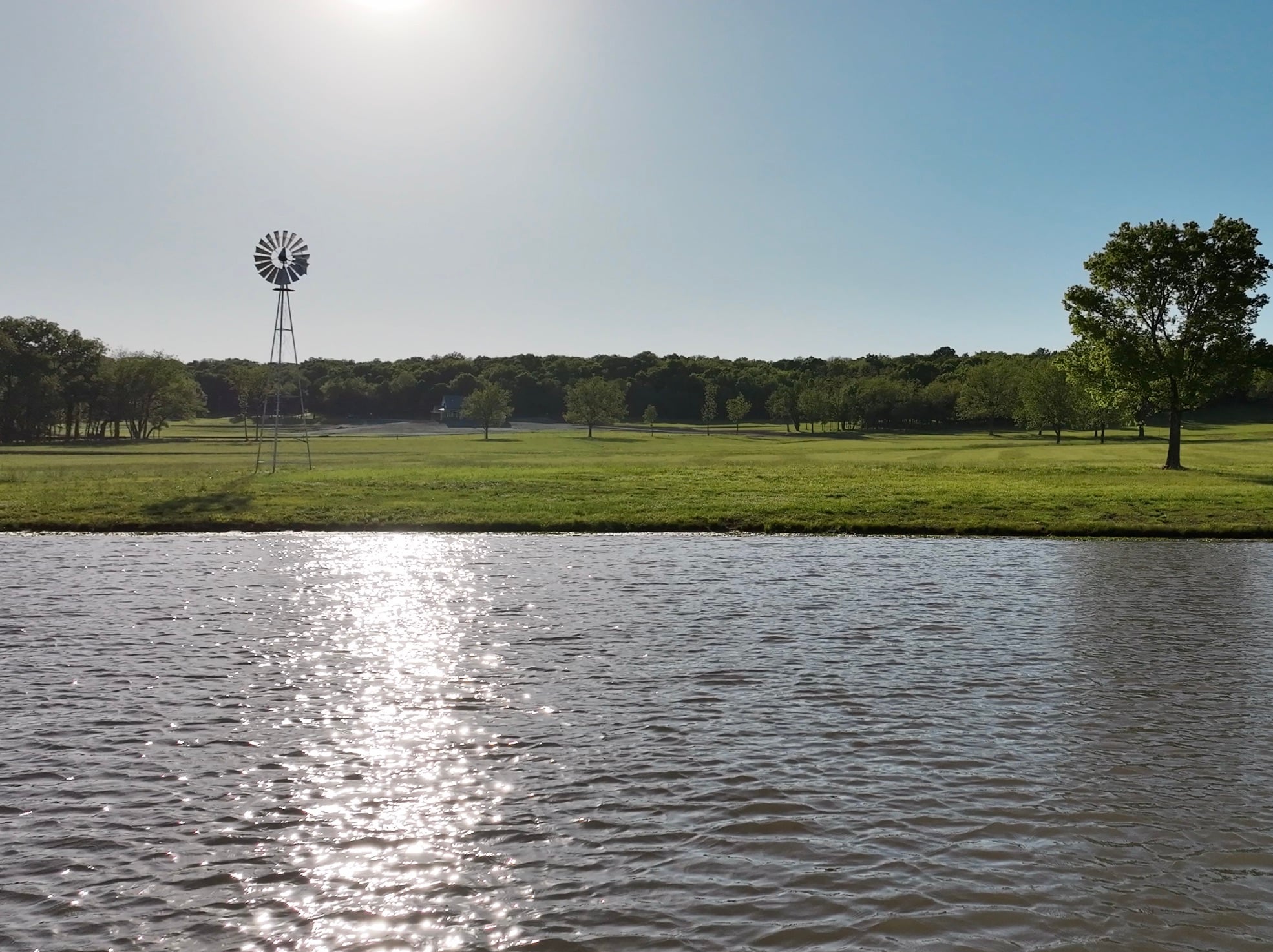 Rebuilt and expanded recreational fishing pond in Centerville, Kansas with a windmill aerator on the bank and mowed lawn beyond